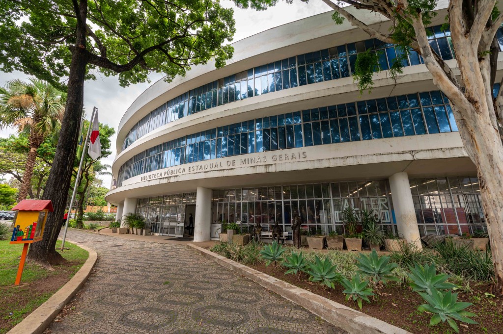 Foto do prédio da biblioteca pública estadual, uma construção modernista com três andares, janelas de vidro e jardins ao redor